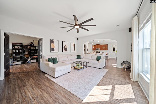 living room featuring arched walkways, ceiling fan, dark wood-style floors, and visible vents