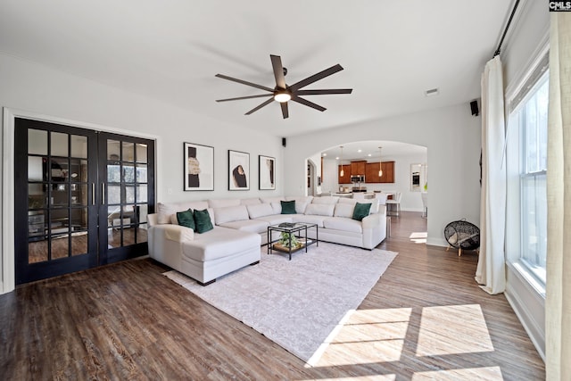 living room with arched walkways, visible vents, a ceiling fan, french doors, and dark wood-style floors