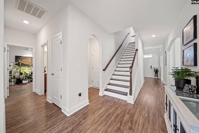 interior space featuring arched walkways, wood finished floors, visible vents, baseboards, and stairs