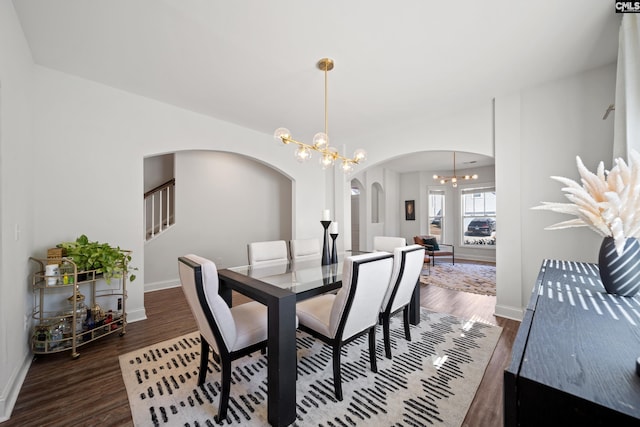 dining room with arched walkways, wood finished floors, baseboards, stairs, and an inviting chandelier