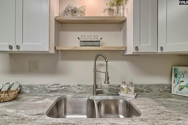 room details featuring open shelves, a sink, white cabinetry, and light stone countertops