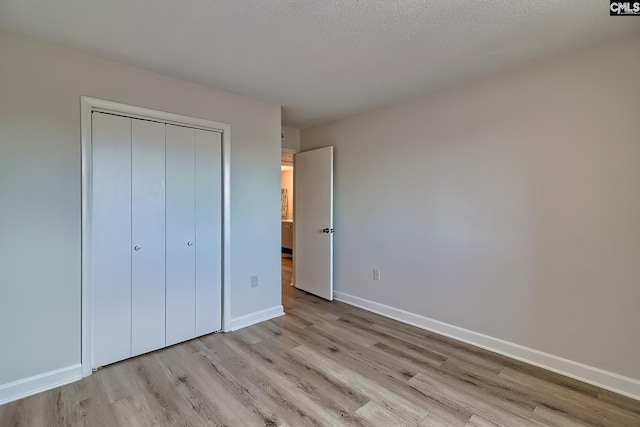 unfurnished bedroom with a textured ceiling, light wood finished floors, a closet, and baseboards