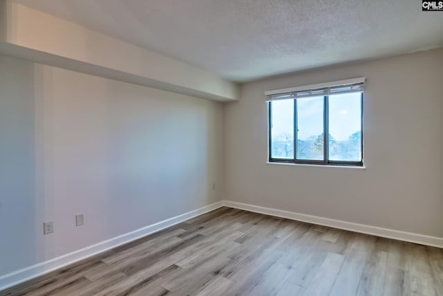 spare room with a textured ceiling, wood finished floors, and baseboards