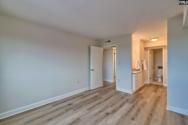 unfurnished bedroom with light wood-style floors, baseboards, visible vents, and connected bathroom