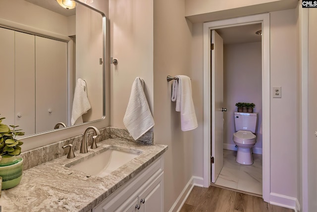 bathroom with toilet, wood finished floors, vanity, and baseboards