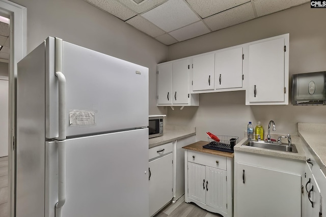 kitchen with a drop ceiling, a sink, white cabinetry, freestanding refrigerator, and stainless steel microwave