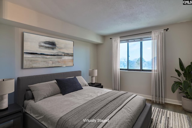 bedroom with a textured ceiling, baseboards, and wood finished floors