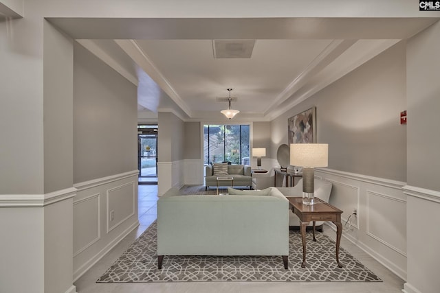 living room with ornamental molding, a raised ceiling, wainscoting, and a decorative wall