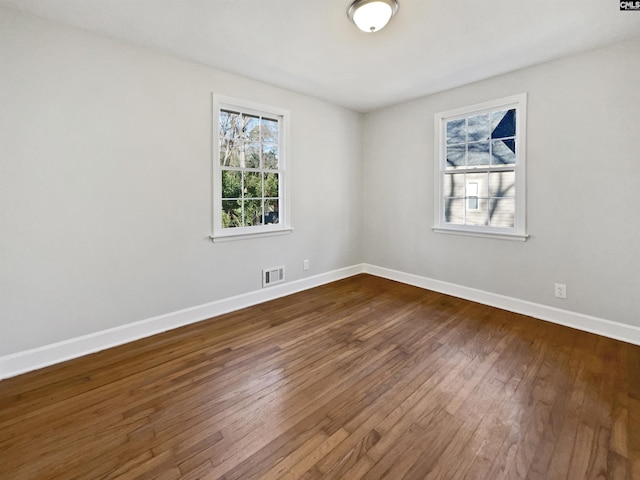 empty room featuring dark wood-style flooring, visible vents, and baseboards