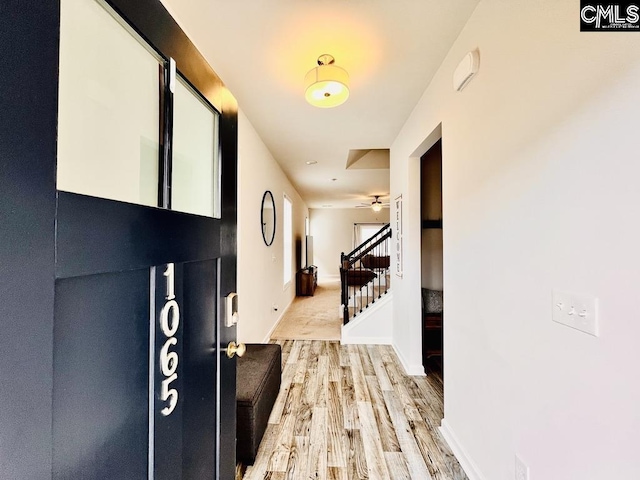 corridor featuring light wood-style floors, baseboards, and stairway