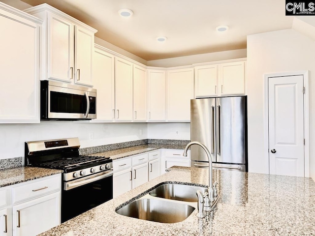 kitchen with light stone counters, appliances with stainless steel finishes, white cabinets, and a sink