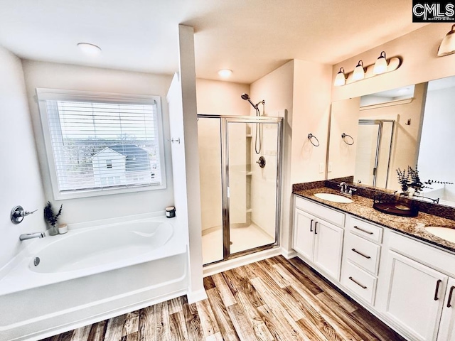 full bathroom featuring double vanity, wood finished floors, a garden tub, a shower stall, and a sink