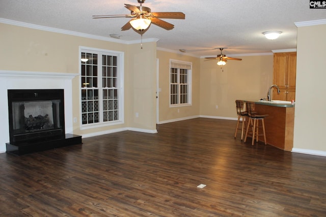 unfurnished living room with a fireplace with raised hearth, a textured ceiling, dark wood-type flooring, a ceiling fan, and ornamental molding