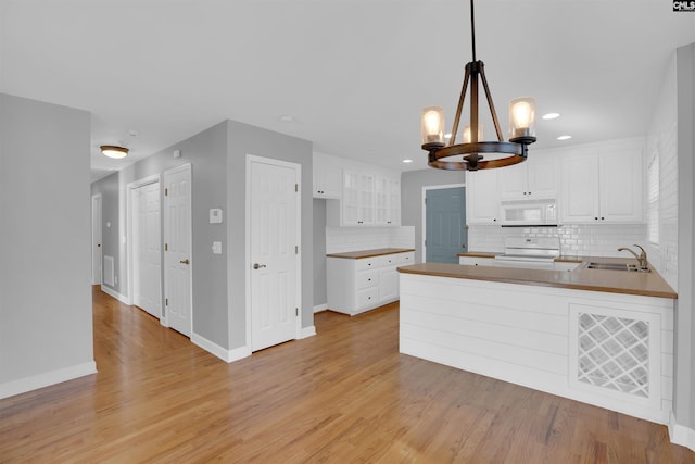 kitchen featuring backsplash, white microwave, a peninsula, light wood-type flooring, and range with electric cooktop