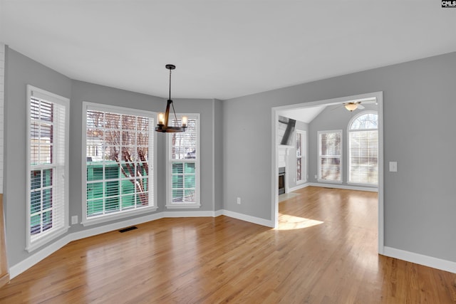 unfurnished dining area featuring visible vents, baseboards, a fireplace with flush hearth, light wood-style flooring, and ceiling fan with notable chandelier