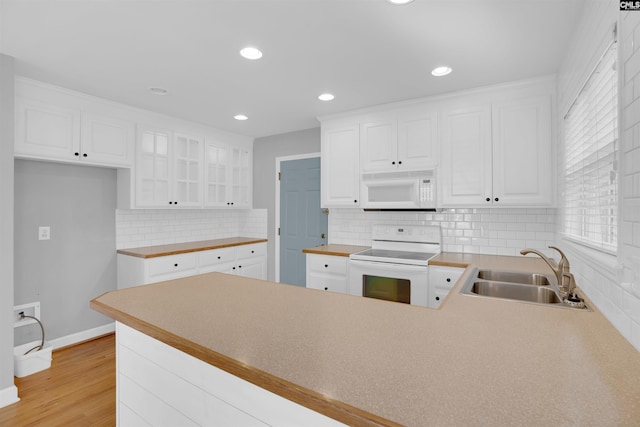 kitchen with white cabinets, a sink, light wood-type flooring, white appliances, and a peninsula