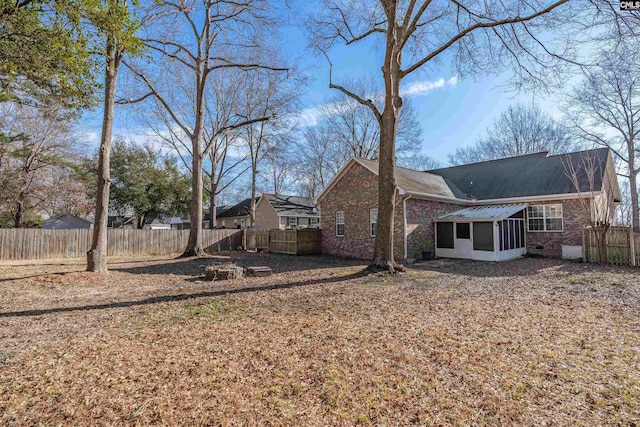 rear view of house with a sunroom, brick siding, and fence