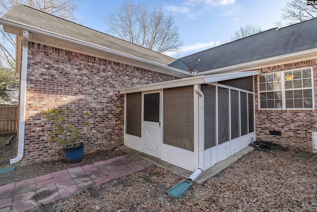 exterior space with brick siding, fence, a sunroom, roof with shingles, and crawl space