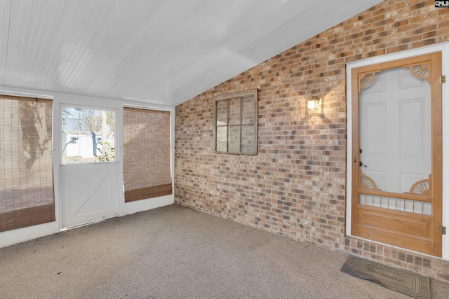 carpeted spare room with vaulted ceiling and brick wall