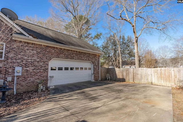 view of property exterior with driveway, a garage, a shingled roof, fence, and brick siding