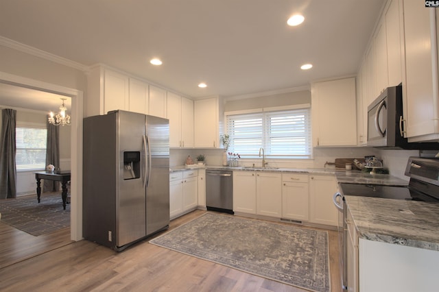 kitchen with stainless steel appliances, a sink, white cabinets, and crown molding