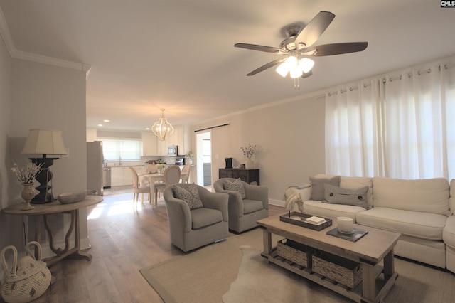 living area with ornamental molding, light wood-style flooring, baseboards, and ceiling fan with notable chandelier