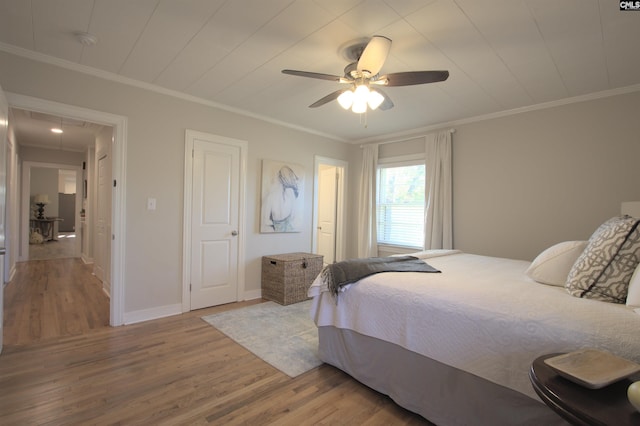 bedroom featuring attic access, baseboards, a ceiling fan, wood finished floors, and crown molding