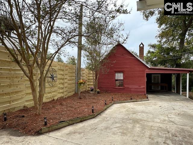 view of side of home with an attached carport, driveway, a chimney, and fence