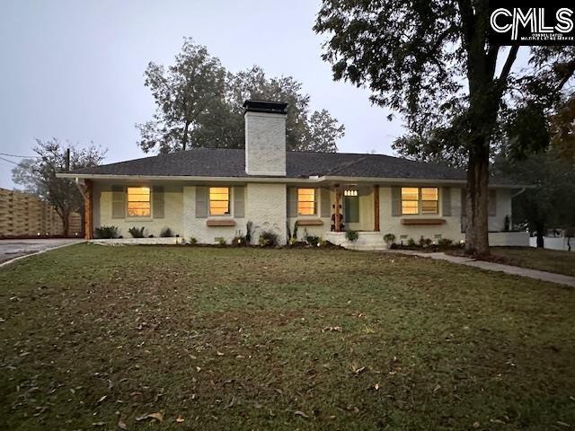 ranch-style home with a chimney, fence, and a front lawn