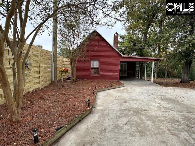 view of side of property with driveway, an attached carport, a chimney, and fence