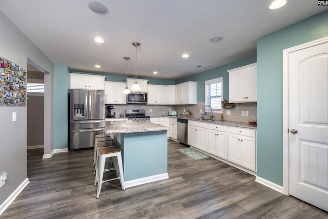 kitchen with decorative backsplash, appliances with stainless steel finishes, white cabinetry, a sink, and a kitchen island