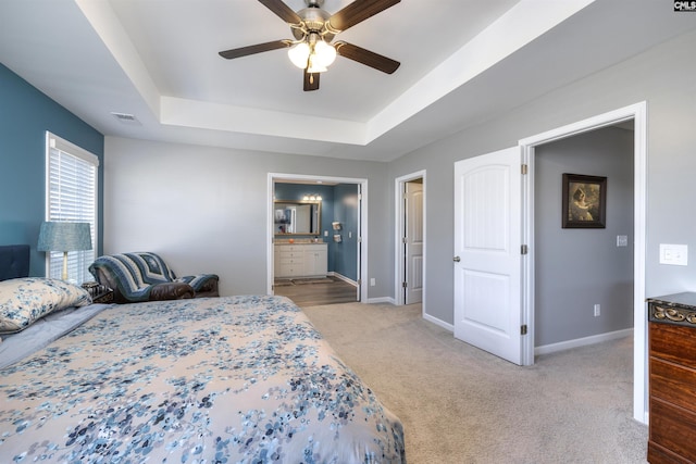 carpeted bedroom with visible vents, baseboards, a raised ceiling, ceiling fan, and ensuite bathroom