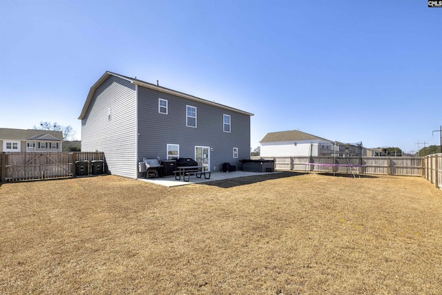 back of house with a trampoline, a fenced backyard, a patio, and a lawn