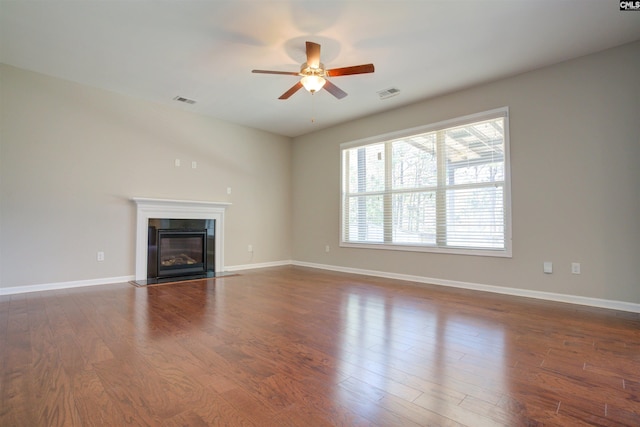 unfurnished living room with ceiling fan, visible vents, dark wood finished floors, baseboards, and a glass covered fireplace