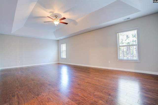 spare room with a tray ceiling, wood finished floors, visible vents, and baseboards