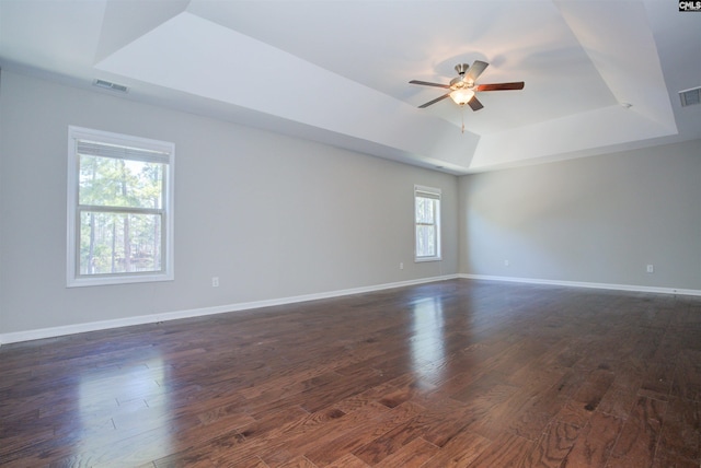unfurnished room with a tray ceiling, dark wood-type flooring, a ceiling fan, and baseboards