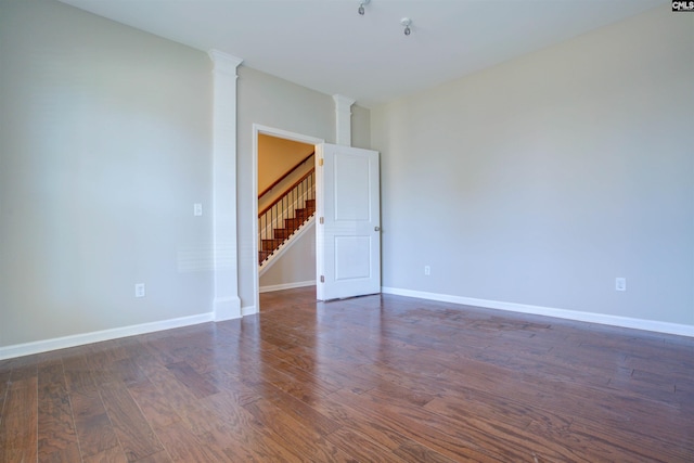 unfurnished room featuring ornate columns, stairs, baseboards, and dark wood finished floors