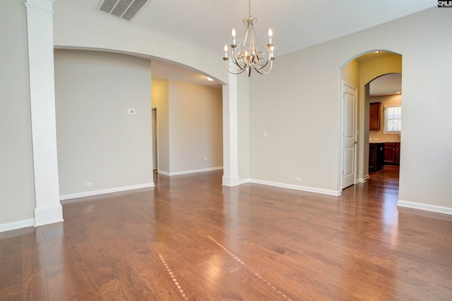 unfurnished room with dark wood-style floors, arched walkways, visible vents, and baseboards