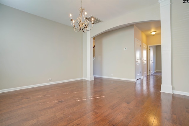empty room featuring dark wood-style floors, baseboards, arched walkways, and a notable chandelier