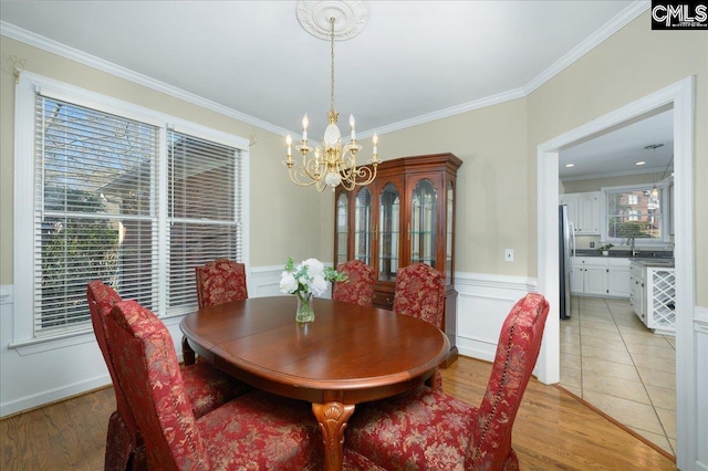 dining room featuring a chandelier, wainscoting, crown molding, and light wood-style flooring