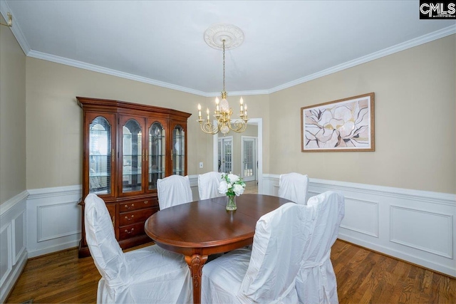 dining area featuring a chandelier, a wainscoted wall, dark wood finished floors, and crown molding