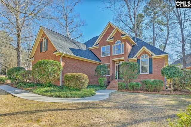 view of front of house with roof with shingles, a front yard, and brick siding