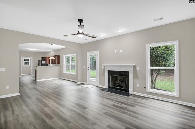 unfurnished living room with baseboards, visible vents, a fireplace with raised hearth, ceiling fan, and dark wood-type flooring