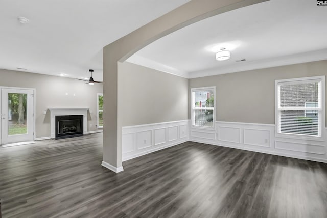 unfurnished living room with arched walkways, ceiling fan, a fireplace with flush hearth, and dark wood-style floors