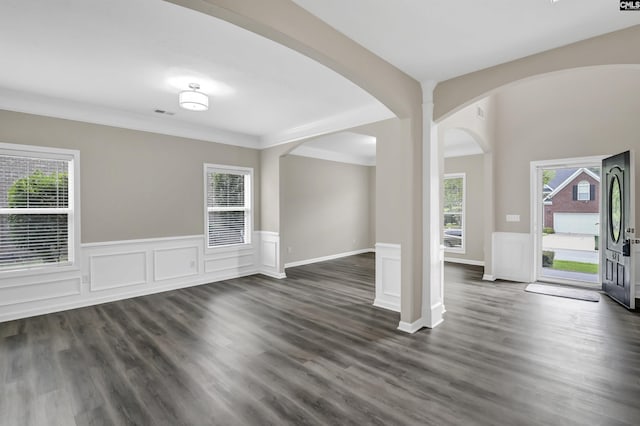 empty room with a wainscoted wall, arched walkways, and dark wood-style flooring