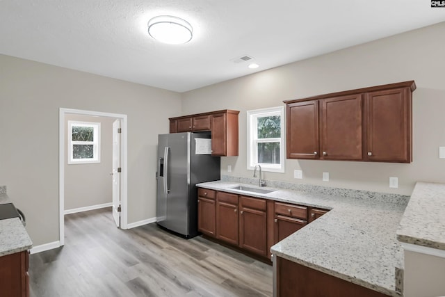 kitchen featuring light stone counters, stainless steel refrigerator with ice dispenser, visible vents, a sink, and baseboards