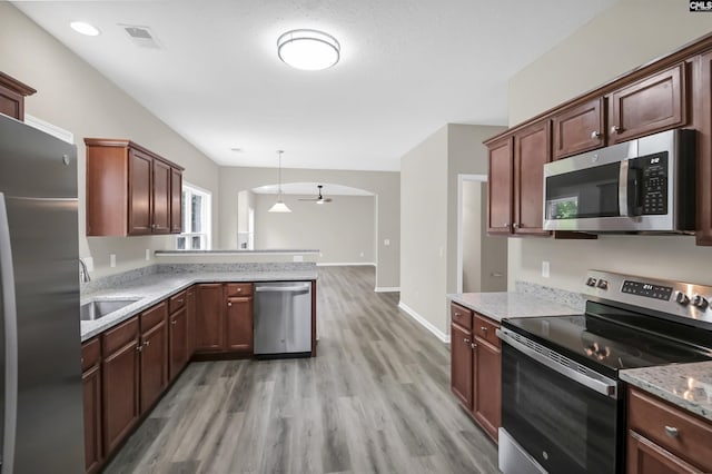 kitchen featuring a peninsula, light wood-style flooring, arched walkways, and stainless steel appliances