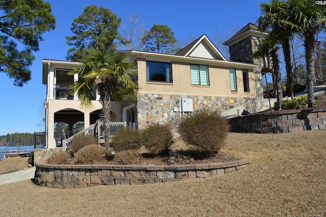 view of front facade featuring stone siding, brick siding, stairway, and a balcony