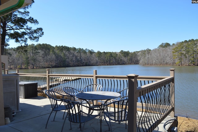 dock area with outdoor dining space, a water view, and a view of trees