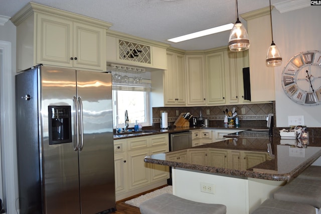 kitchen with stainless steel appliances, cream cabinetry, decorative backsplash, and dark stone countertops